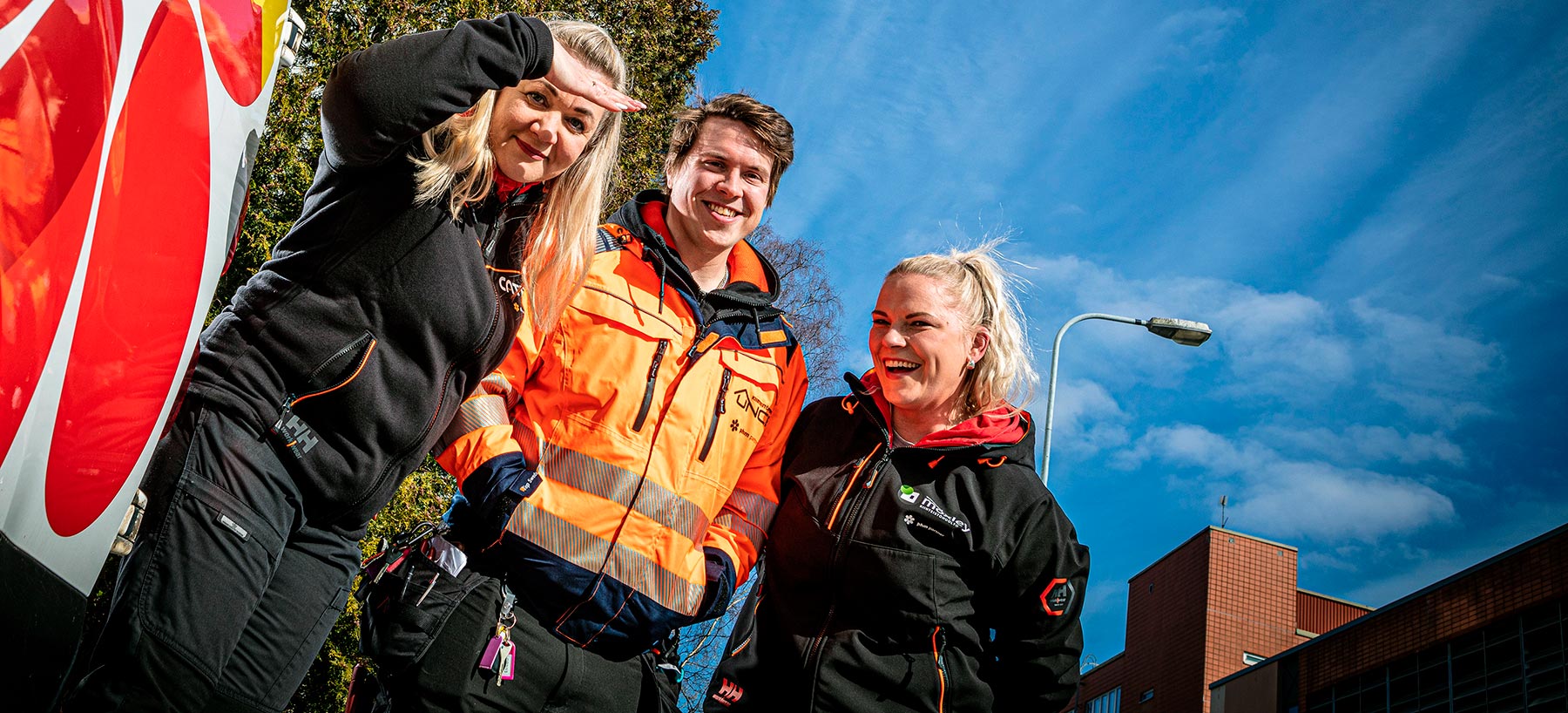 Two women and a man smile at the camera in front of a van